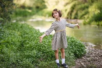 Girl gesturing while standing on field by lake