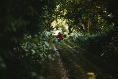 Rear view of girl running on footpath amidst trees