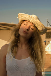 Young woman with eyes closed wearing hat against clear sky