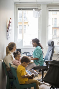 Smiling pediatrician talking to mother while children sitting in clinic