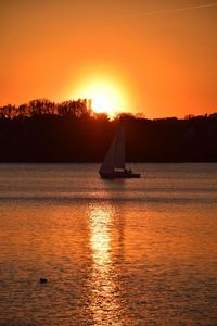 Silhouette sailboat sailing on sea against orange sky