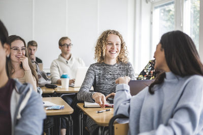 Smiling female friends talking while sitting in classroom