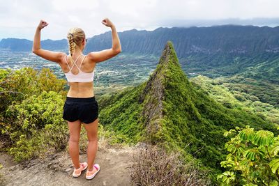 Rear view of young woman gesturing while standing on mountain against sky