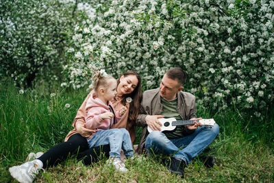 Family mom mom baby daughter in the garden blooming apple trees, father playing the ukulele