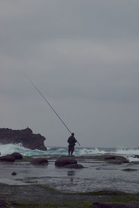 Man fishing in sea against clear sky