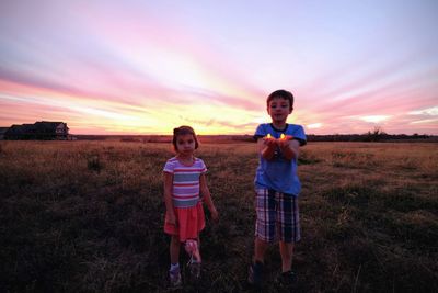 Boy holding lit candles while standing with sister on grassy field at dusk