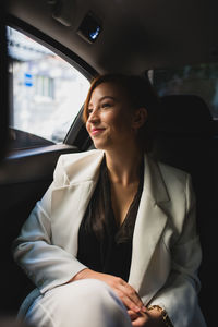 Content businesswoman in elegant suit sitting on passenger seat in taxi and commuting to work while looking out of window
