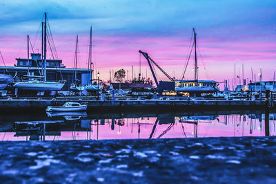 Sailboats moored at harbor against sky during sunset