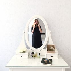 Young woman taking selfie with smart phone reflecting on mirror at home