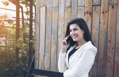 Young woman using phone while standing on wood
