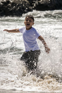 Full length of shirtless man splashing water in sea