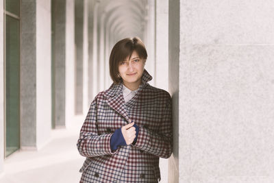 Portrait of smiling young woman standing against wall