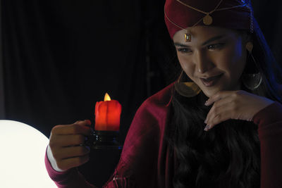 Female fortune teller with burning candle against black background