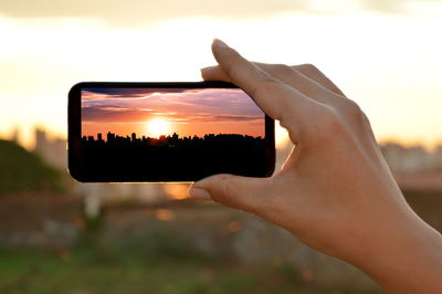 Close-up of woman using mobile phone against sunset sky