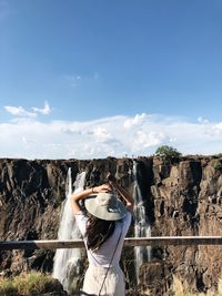 Rear view of woman standing by railing against waterfall