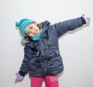 Portrait of smiling girl wearing warm clothing with arms outstretched against white background