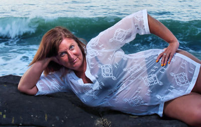 Portrait of mature woman lying on rock formation against sea