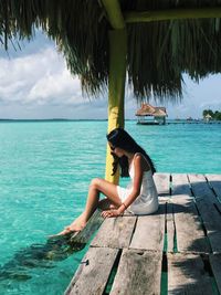 Side view of woman sitting on pier over sea against sky