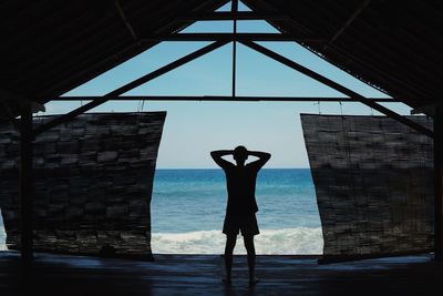 Silhouette man standing in hut at sea shore against sky