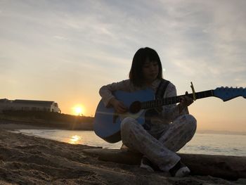 Man playing guitar at beach against sky during sunset