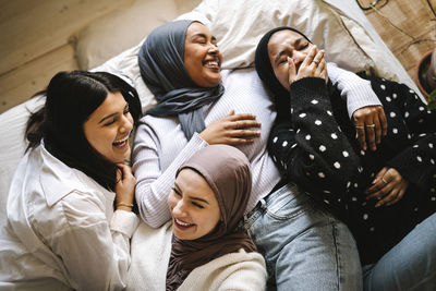 Young female friends in hijabs laughing while enjoying on bed at home