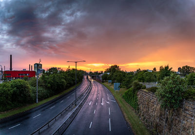 Road by trees against sky during sunset