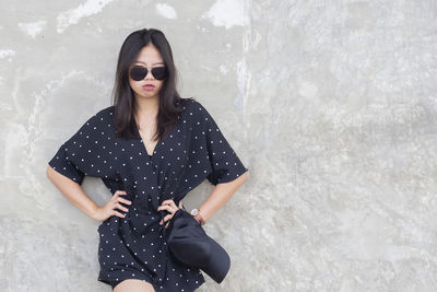 Young woman wearing sunglasses standing against wall