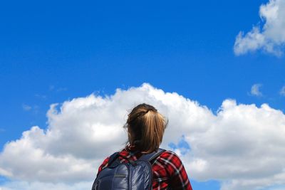 Rear view of backpack woman standing against blue sky