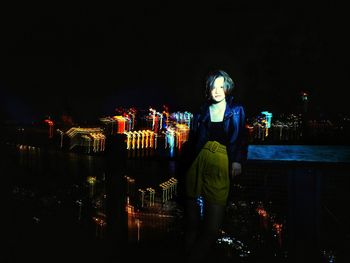 Woman standing by illuminated cityscape against sky at night