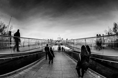 People on bridge against cloudy sky