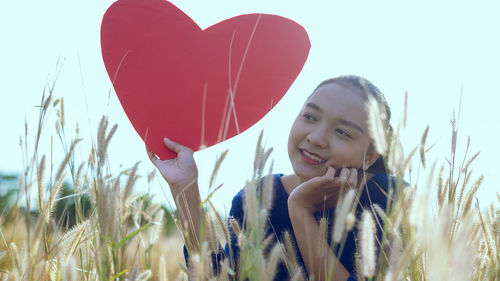 Portrait of happy woman with heart shape on field against sky