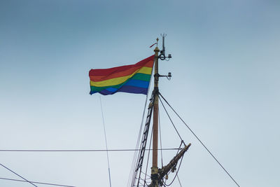 Low angle view of rainbow flag waving on mast of sailboat against clear blue sky