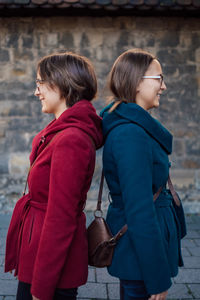 Smiling sisters standing back to back against stone wall