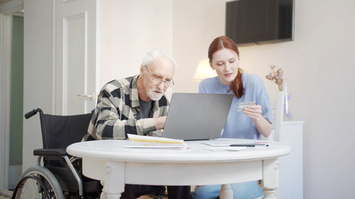 Caregiver with senior man using laptop at home