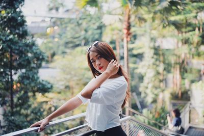 Portrait of woman standing by railing against trees