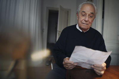 Senior man sitting at table at home reading a paper