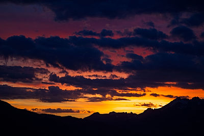 Scenic view of dramatic sky over silhouette mountains during sunset