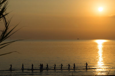Silhouette people in sea against sky during sunset