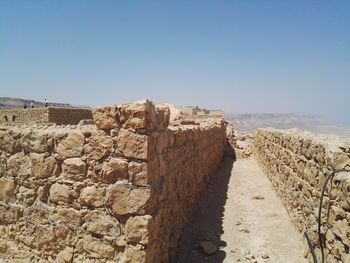Stone wall by sea against clear blue sky