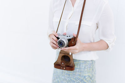 Midsection of woman with camera standing against white background