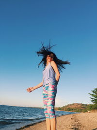 Low angle view of woman tossing hair while standing at beach against sky