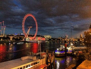 Illuminated ferris wheel by river against sky at night