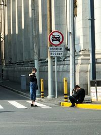 Full length of man with road sign on street in city