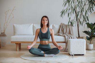 A young woman practices yoga at home in a tracksuit. sitting in the lotus position