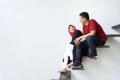 Portrait of smiling young couple sitting against white background