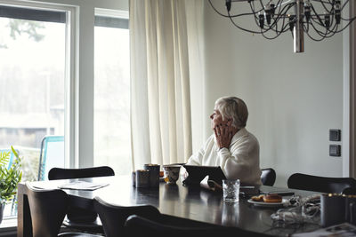 Senior woman looking away while sitting by dining table at home