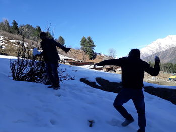 Rear view of men standing on snow field against sky