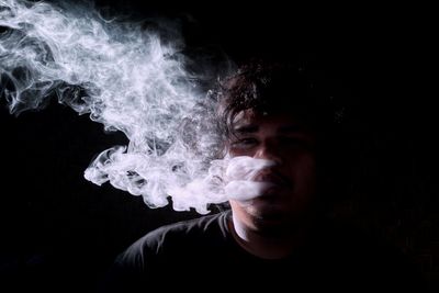 Close-up portrait of man smoking over black background