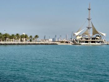 Sailboats in sea by buildings against clear blue sky