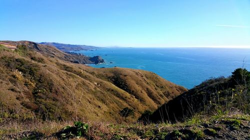 Scenic view of mountain by sea against clear blue sky